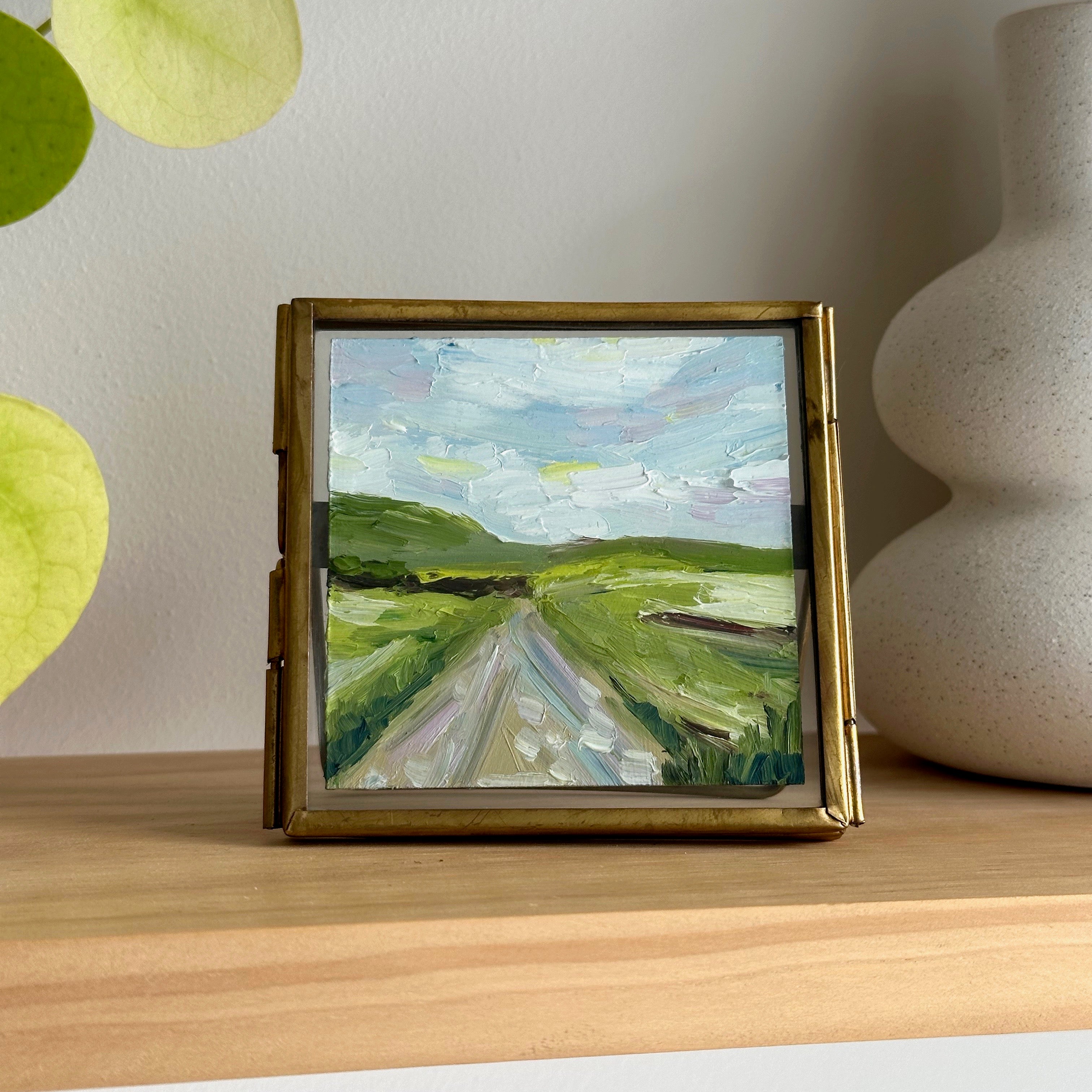 Framed painting of a landscape with rolling hills on a wooden surface.