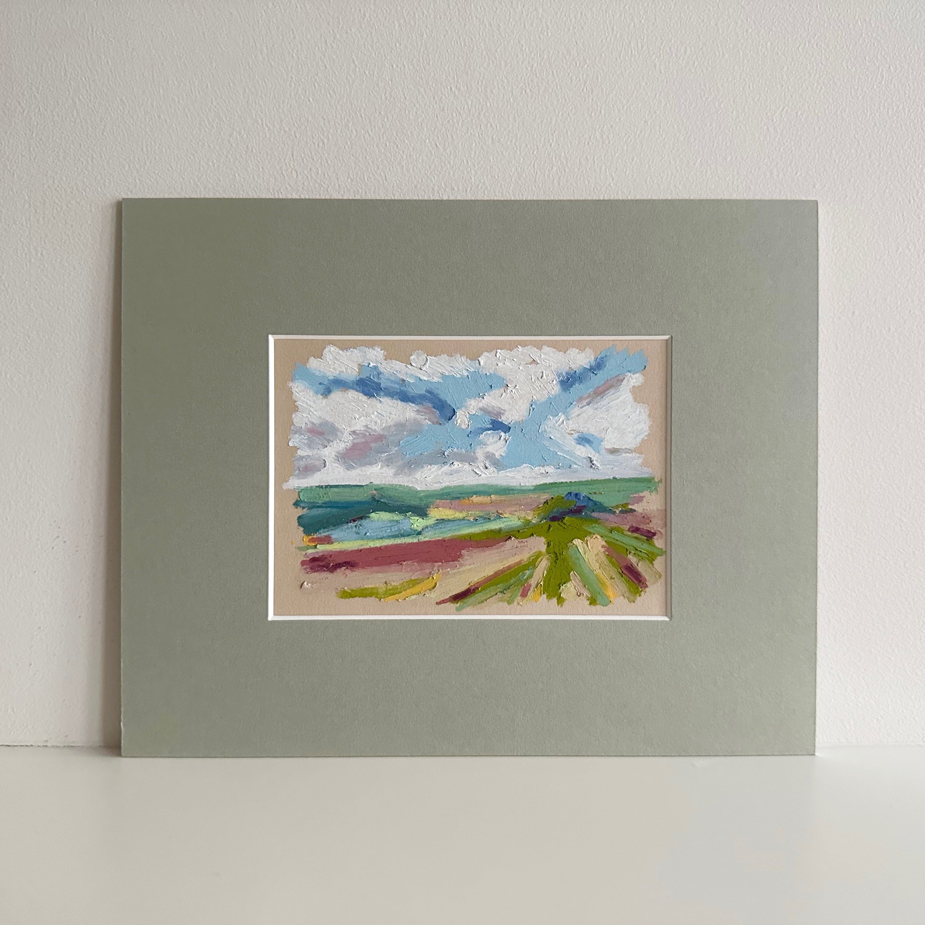 Small landscape painting with a colourful sky and fields in a sage green mount.