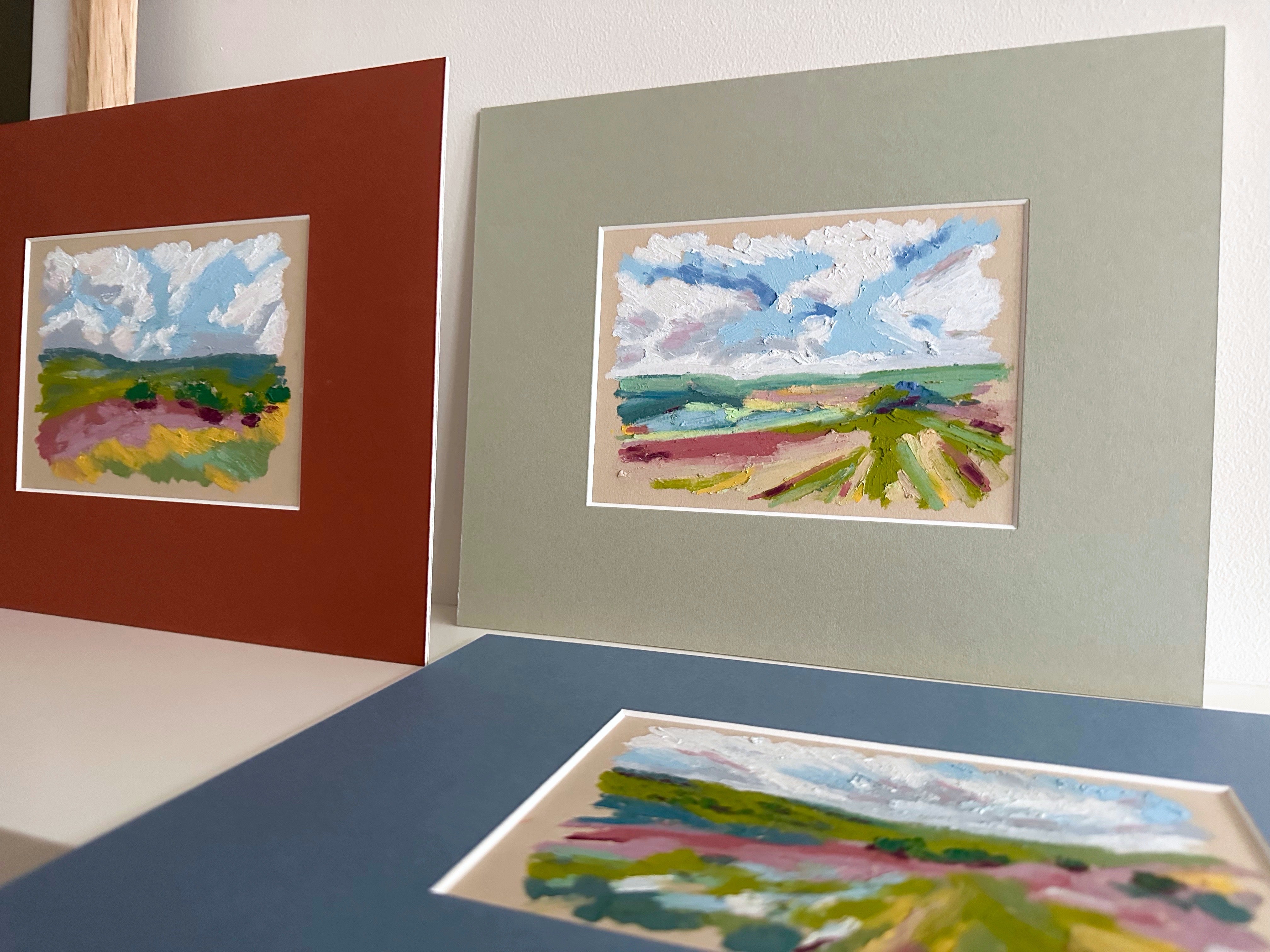 Three framed artworks of landscapes on a shelf with a neutral background